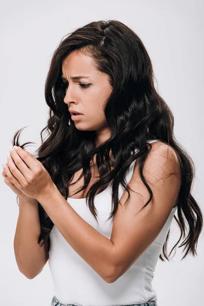 Upset brunette beautiful woman looking at damaged hair isolated on grey — Stock Photo