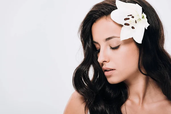 Morena hermosa mujer con los ojos cerrados y lirio en el pelo largo y saludable aislado en gris - foto de stock