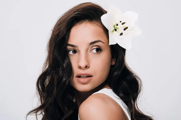 Brunette beautiful woman with lily in long healthy hair looking away isolated on grey — Stock Photo