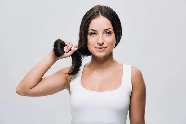 Brünette schöne Frau hält lange gerade gesunde und glänzende Haare isoliert auf grau — Stockfoto