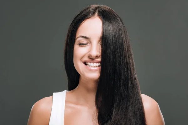 Счастливая брюнетка красивая женщина с длинными прямыми здоровыми и блестящими волосами изолированы на сером — стоковое фото