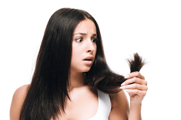 Scared brunette beautiful woman looking at long straight damaged hair isolated on white — Stock Photo