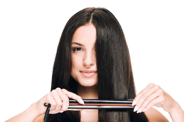 Brunette beautiful woman straightening long shiny hair with flat iron isolated on white — Stock Photo