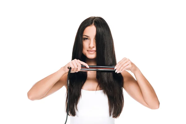 Brunette beautiful woman straightening long shiny hair with flat iron isolated on white — Stock Photo