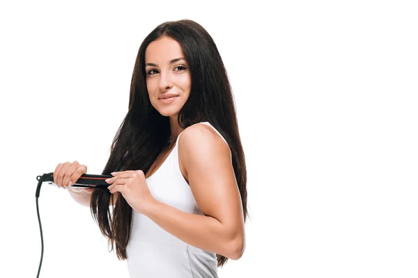 Side view of brunette beautiful woman straightening long shiny hair with flat iron isolated on white — Stock Photo