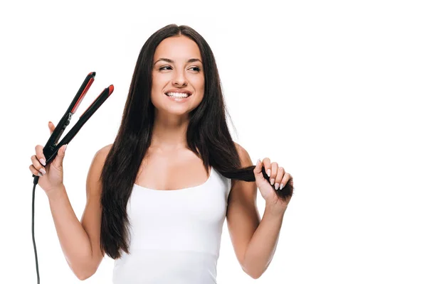 Happy brunette beautiful woman straightening long shiny hair with flat iron isolated on white — Stock Photo