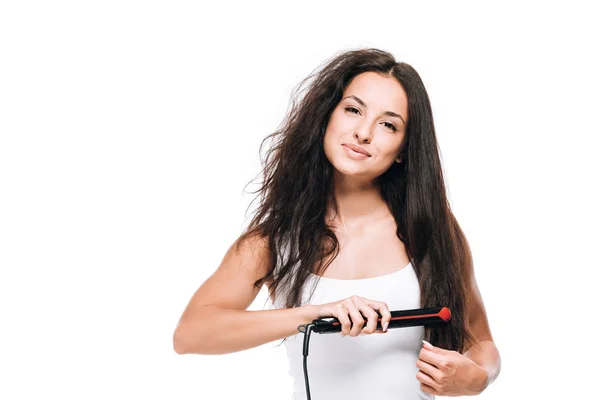 Brune souriante belle femme coiffant cheveux raides et bouclés avec fer plat isolé sur blanc — Photo de stock