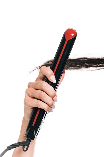 Partial view of woman styling curly hair with flat iron isolated on white — Stock Photo