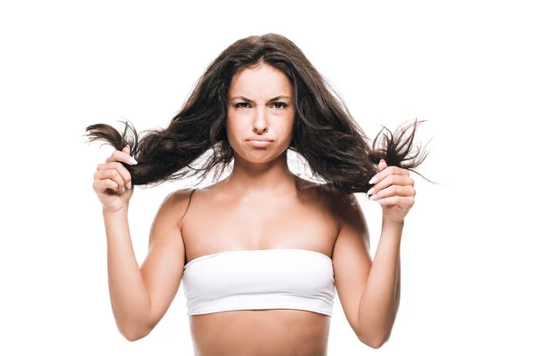 Upset brunette beautiful woman holding curly hair isolated on white — Stock Photo