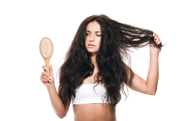 Worried brunette beautiful woman with wavy unruly hair looking at comb isolated on white — Stock Photo