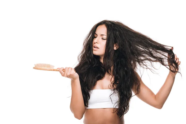 Bouleversé brunette belle femme aux cheveux ondulés indisciplinés regardant peigne isolé sur blanc — Photo de stock