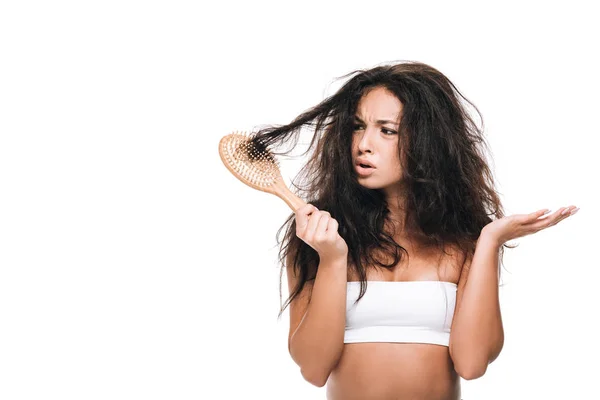 Femme brune stressée regardant ondulé cheveux indisciplinés dans peigne isolé sur blanc — Stock Photo