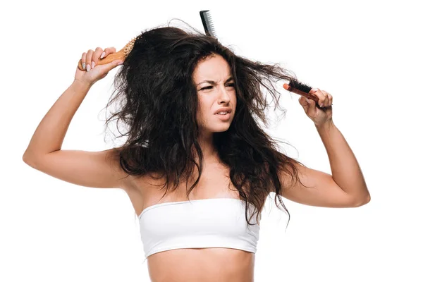 Worried brunette woman with combs in wavy unruly hair isolated on white — Stock Photo