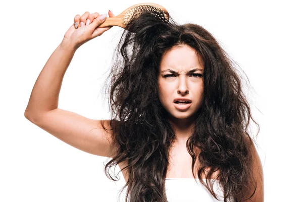 Mulher morena confusa styling cabelo encaracolado indisciplinado com escova de cabelo isolada no branco — Fotografia de Stock