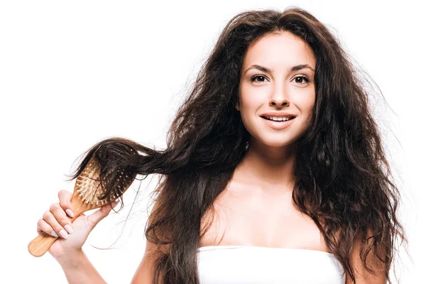 Smiling brunette woman styling curly hair with hairbrush isolated on white — Stock Photo