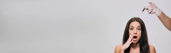 Colpo panoramico di cosmetologo in guanti di lattice facendo mesoterapia del cuoio capelluto per scioccato bella donna con i capelli lunghi isolati su grigio — Foto stock