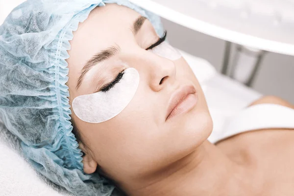 Modelo con pestañas postizas y ojos cerrados acostados en el sofá durante el procedimiento - foto de stock