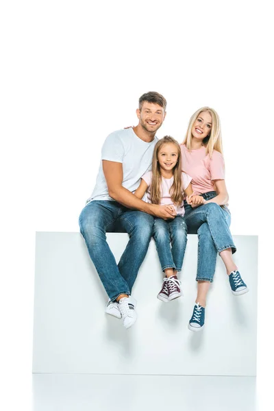 Happy parents and daughter sitting on cube isolated on white — Stock Photo