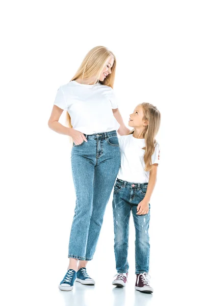 Hermosa madre de pie con la mano en el bolsillo cerca de hija preadolescente en blanco - foto de stock