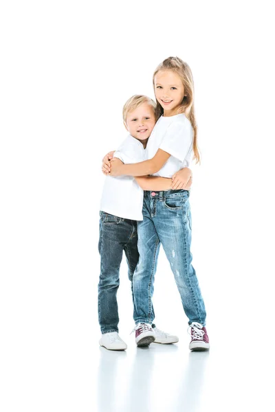 Счастливый ребенок обнимает веселого брата, стоя на белом — стоковое фото