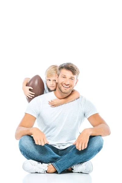 Милый мальчик держит мяч для регби и обнимает счастливого отца на белом — стоковое фото