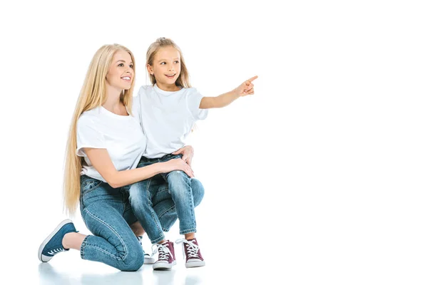 Feliz madre sentada cerca de hija señalando con el dedo en blanco - foto de stock