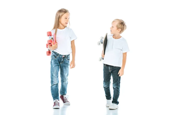 Happy kids smiling while looking at each other and holding penny boards on white — Stock Photo