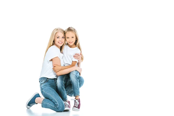 Fröhliche Mutter umarmt glückliche Tochter in blauen Jeans auf weißem Grund — Stockfoto