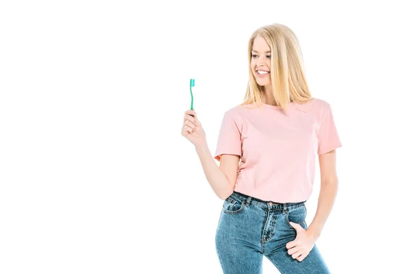 Attractive woman in blue jeans standing and looking at toothbrush isolated on white — Stock Photo