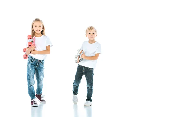 Glückliche Kinder lächeln, während sie in die Kamera schauen und Penny-Bretter auf weiß halten — Stockfoto