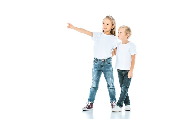 Happy kid in jeans pointing with finger and holding hands with brother on white — Stock Photo