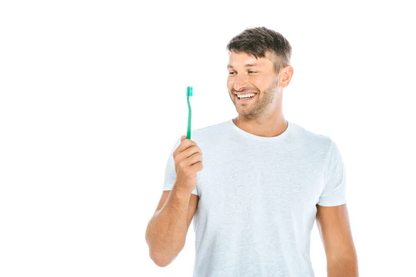 Hombre alegre mirando cepillo de dientes mientras sonríe aislado en blanco - foto de stock