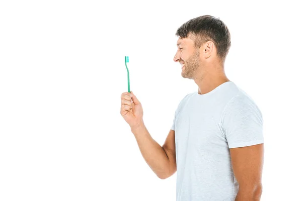 Vista lateral do homem alegre olhando para a escova de dentes enquanto sorrindo isolado no branco — Fotografia de Stock