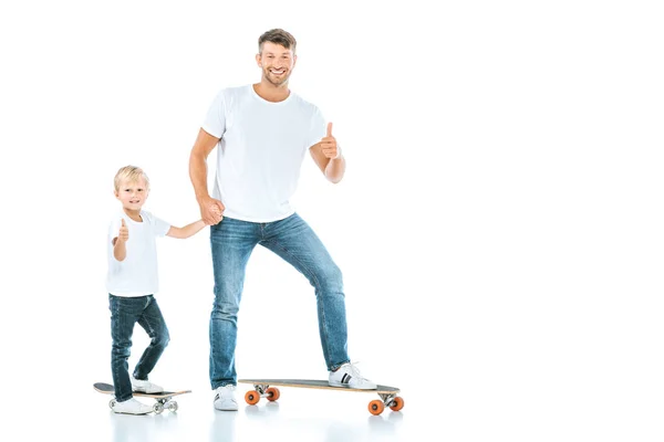 Счастливые отец и сын показывая большие пальцы вверх во время езды на пенни доски изолированы на белом — стоковое фото