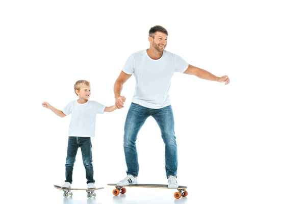 Père positif et fils gai chevauchant planches de penny et tenant les mains isolées sur blanc — Photo de stock