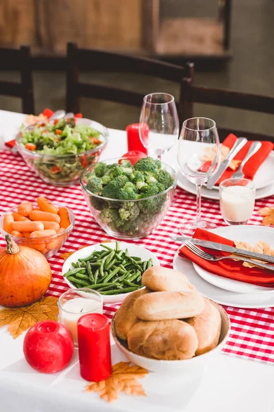 Vista de ángulo alto de la mesa con ensalada, vasos, velas, verduras, pasteles, platos y calabazas en el día de Acción de Gracias - foto de stock