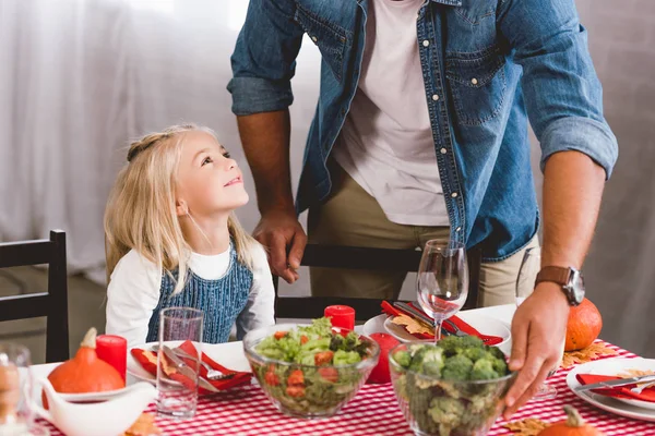 Vue recadrée de père mettant sur la table bol avec brocoli et fille mignonne souriant et le regardant dans le jour de Thanksgiving — Photo de stock