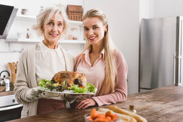Sonriente madre e hija sosteniendo el plato con sabroso pavo en el día de Acción de Gracias - foto de stock