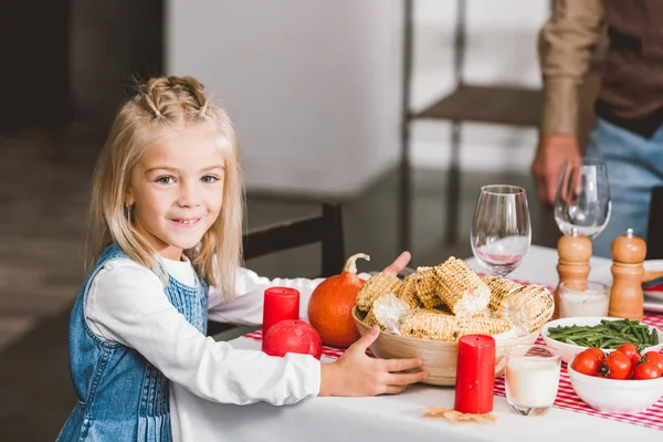 Enfoque selectivo de linda hija sosteniendo tazón con maíz y sonriendo en el día de Acción de Gracias - foto de stock
