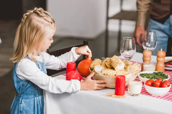 Enfoque selectivo de linda hija sosteniendo tazón con maíz y calabaza en el día de Acción de Gracias - foto de stock