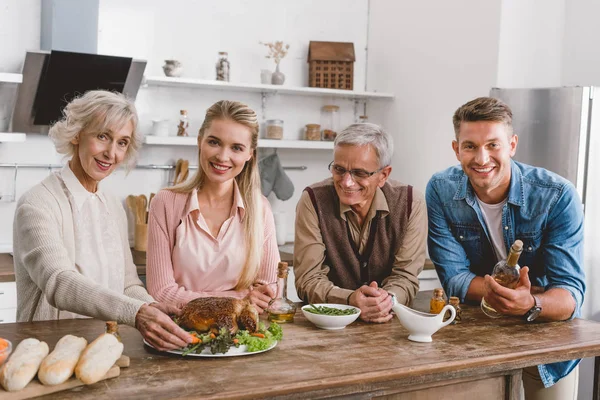 Familiares sonrientes sosteniendo el plato con pavo y mirando a la cámara en el día de Acción de Gracias - foto de stock