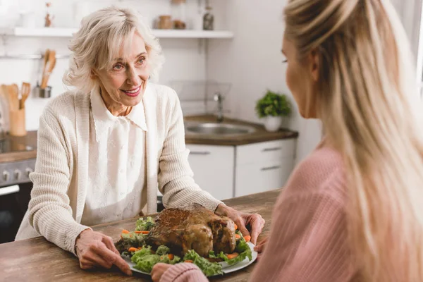 Smiling mother and daughter holding plate with turkey in Thanksgiving day — Stock Photo