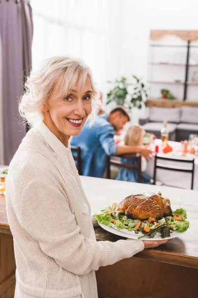 Smiling grandmother holding plate with turkey in Thanksgiving day — Stock Photo