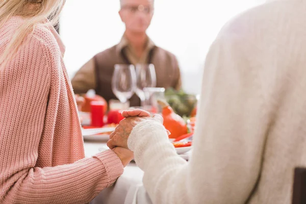 Cropped view of mother and grandmother holding hands and praying in Thanksgiving day — Stock Photo