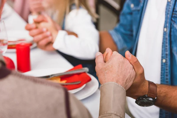 Cropped view of father and grandfather holding hands and prying in Thanksgiving day — Stock Photo