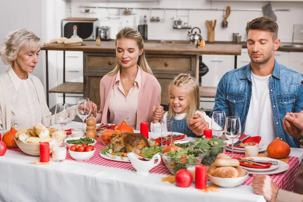 Familia con los ojos cerrados tomados de la mano y entrometiéndose en el día de Acción de Gracias - foto de stock