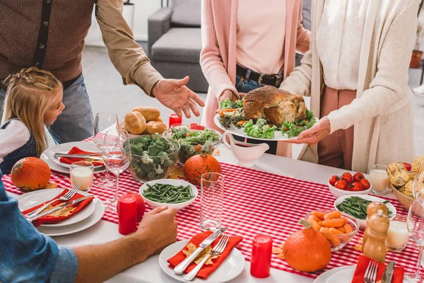 Vista cortada da família sentada à mesa e mãe com a avó segurando prato com peru no dia de Ação de Graças — Fotografia de Stock