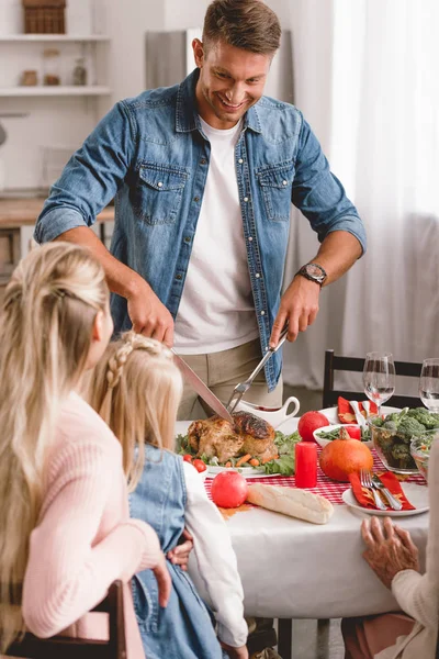 Selective focus of family members sitting at table and father cutting tasty turkey in Thanksgiving day — Stock Photo