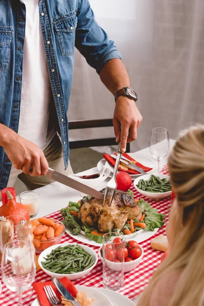 Cropped view of family members sitting at table and father cutting tasty turkey in Thanksgiving day — Stock Photo