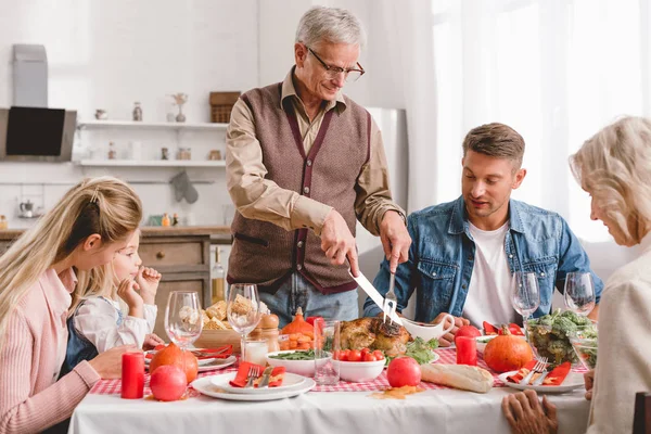 Familienmitglieder sitzen am Tisch und Großvater schneidet schmackhaften Truthahn zum Erntedank — Stockfoto